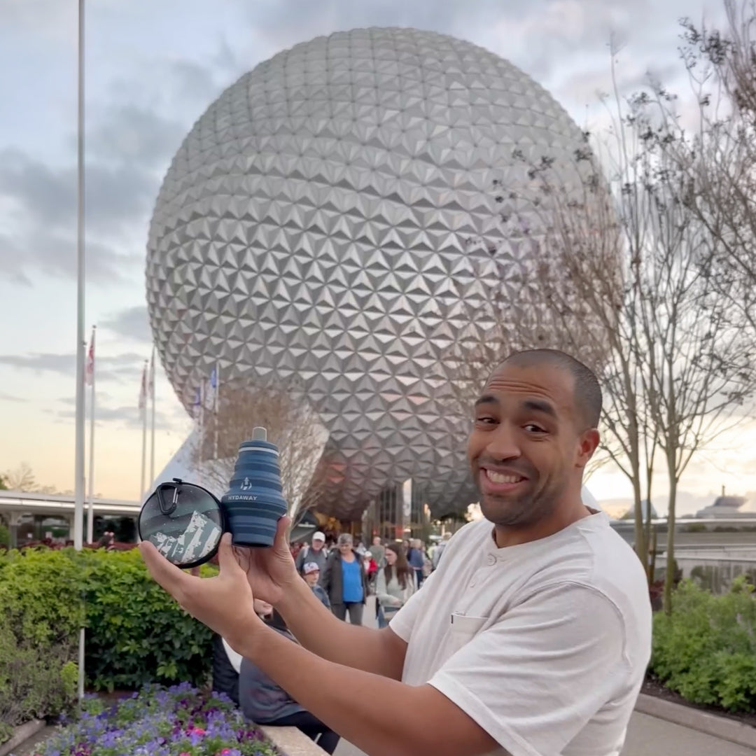 Man holding a HYDAWAY collapsible water bottle and travel case  in front of Epcot's Spaceship Earth at Disney World.