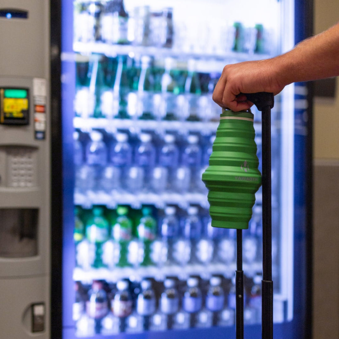 Person using a green HYDAWAY collapsible water bottle in front of a vending machine with Pepsi branding.