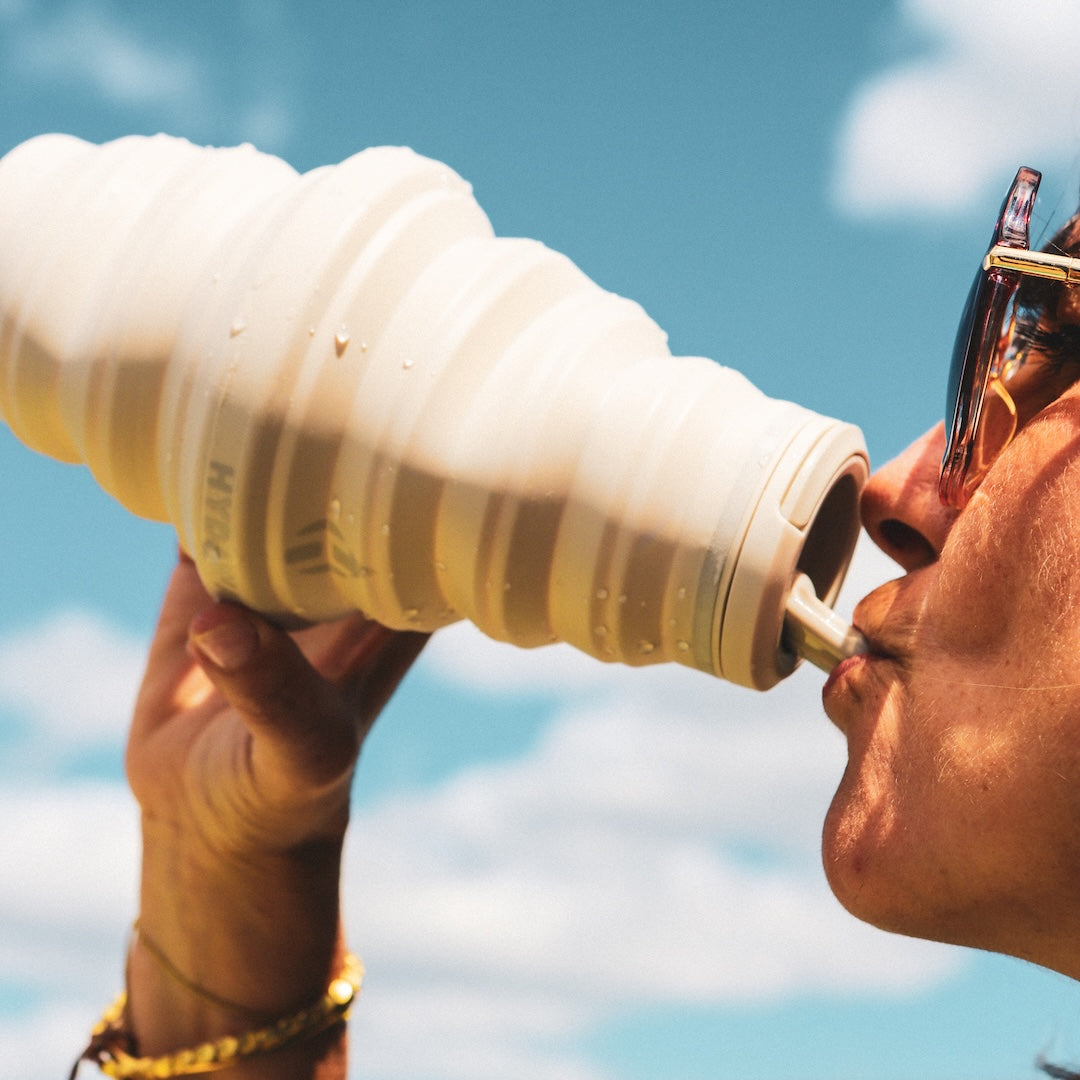 Person drinking from a 25 ounce HYDAWAY collapsible water bottle with a blue sky background